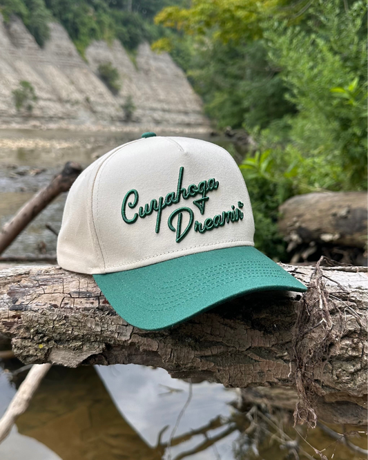 Cap with 'Cuyahoga Dreams' text on a log by a natural waterway